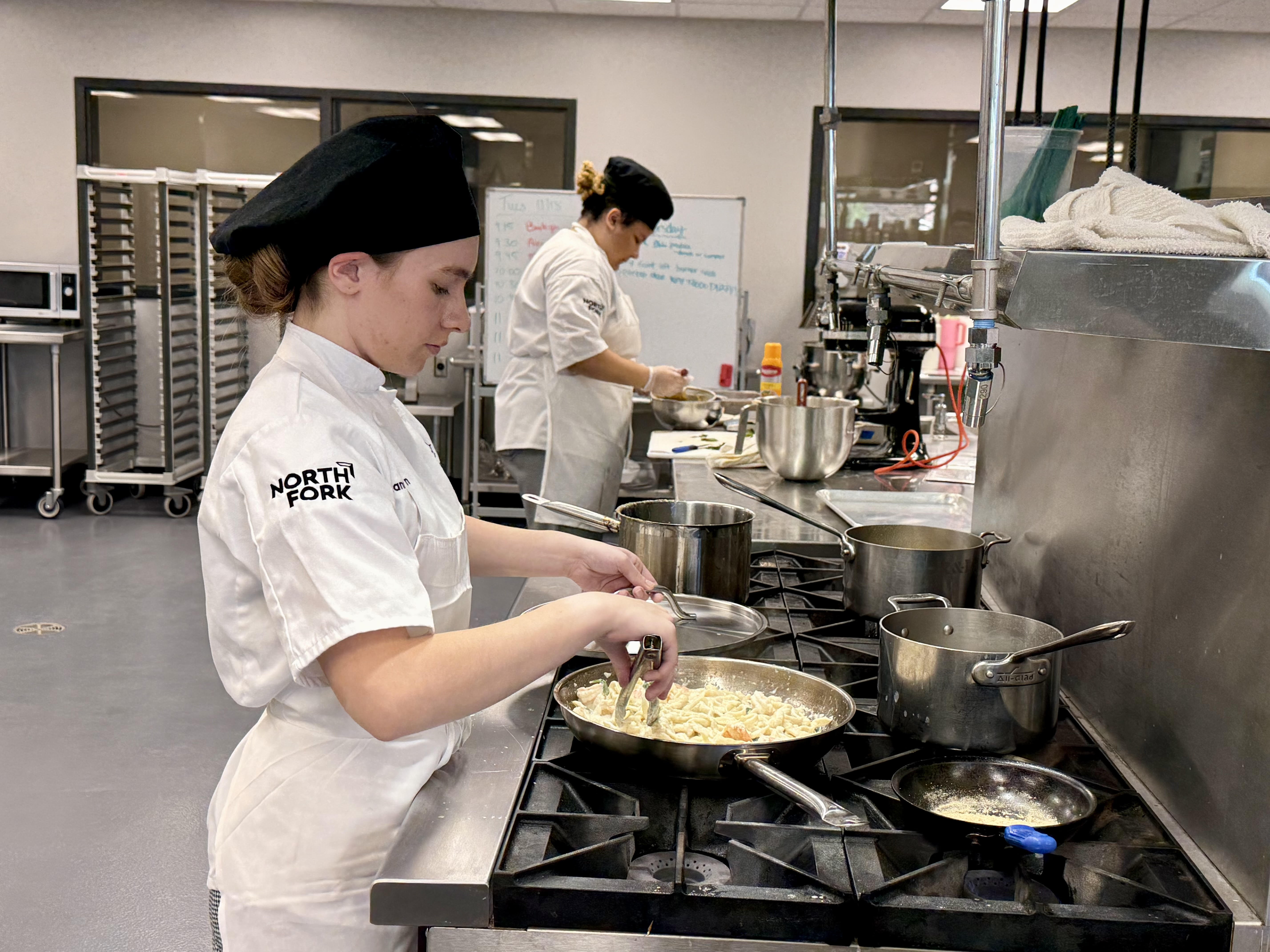 Student Hannah Mason (foreground) prepares a Spinach-Shrimp Alfredo, while Cadence Bell assembles an Orange Spice Cake.