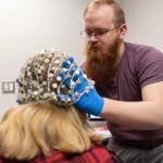 Graduate student Elijah Nieman places the current 64-electrode EEG on a research subject. The new integrated system will feature two high-density EEGs with 256 electrodes each.