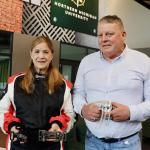 Curt Tucker holds a prototype of the multi-function seat belt buckle being reviewed by NASA. His wife, Korina, models a TEAMTECH racing suit and holds in her left hand the self-tightening over center (STOC) seat belt buckle being reviewed for use in NASCAR races.